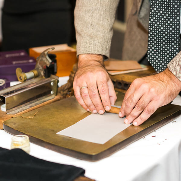 man rolling traditional cigars from tobacco leaves using a mechanical device and press